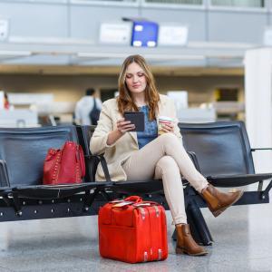 Woman in the airport with a red suitcase. Cheap holiday insurance tips.